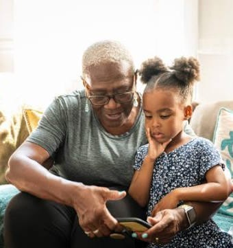 Grandmother showing her young granddaughter something on a phone, connecting across generations